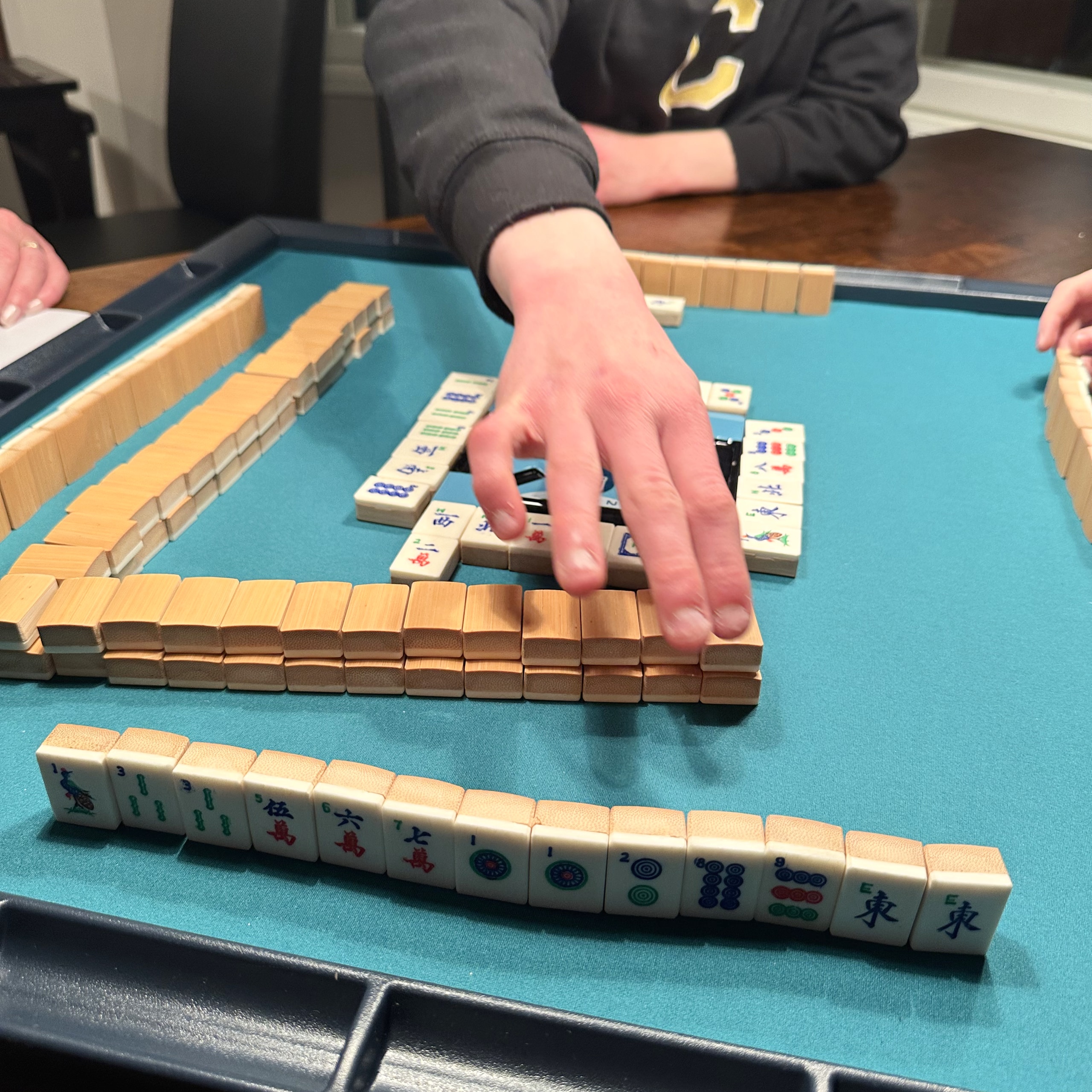 A mahjong player reaching across the table to draw from the wall.