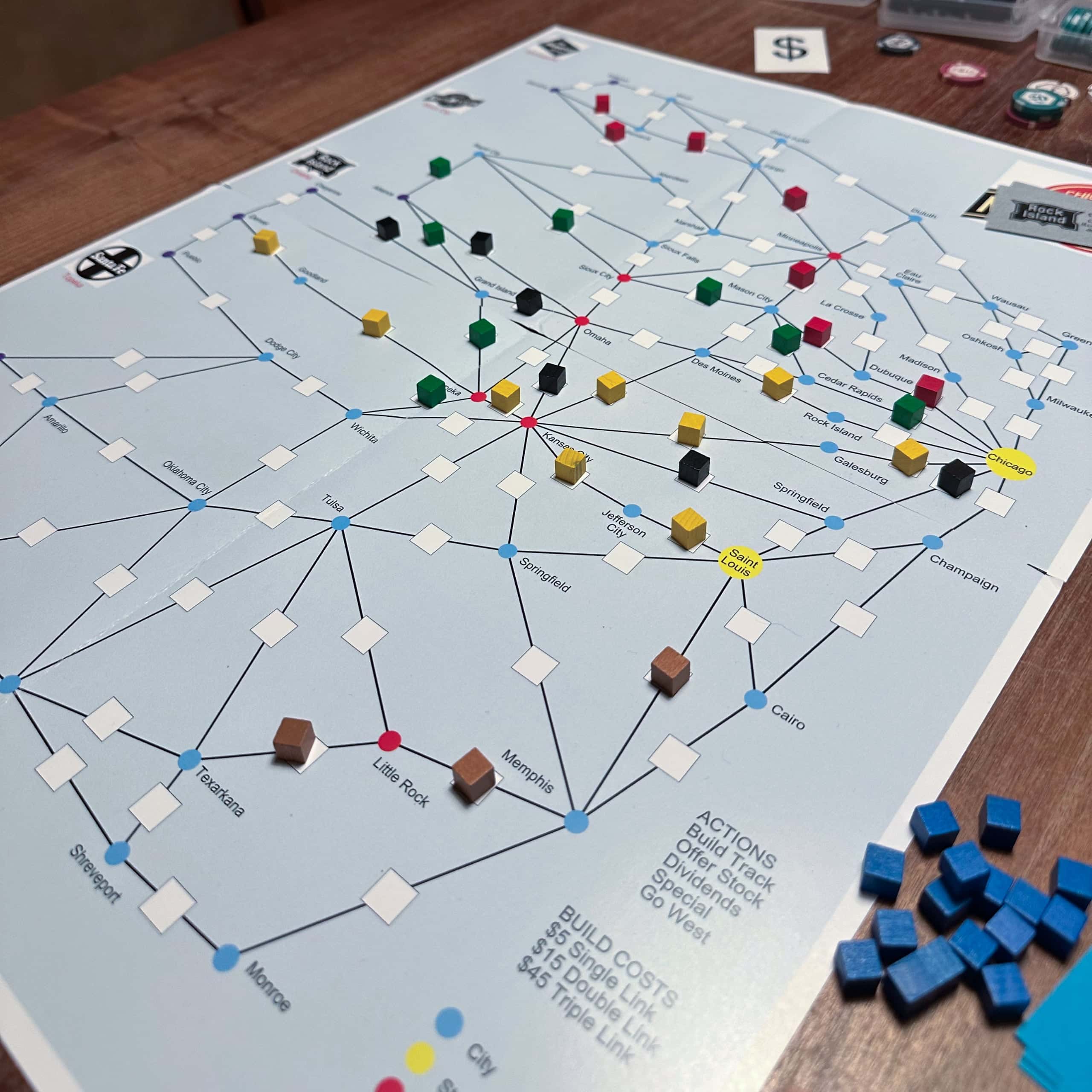 Chicago & NorthWestern board is pale blue, with a graph of lines and nodes depicting rail connections west from Chicago. Each line has a box for a cube, and the board has couple of dozen wooden cubes in various colours showing how the rail networks have spread west from Chicago.